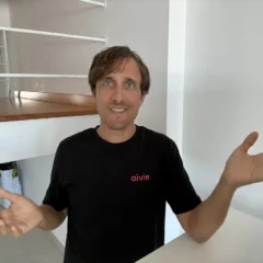 Adrian Schimpf im schwarzen Aivie-T-Shirt hebt fragend beide Hände